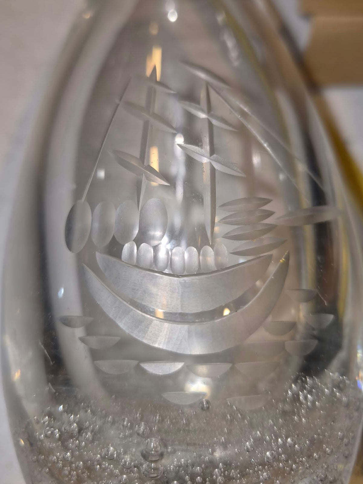 A clear glass decorative vase featuring an etched sailing ship design on the front, photographed close-up with some bubbles visible near the base.
