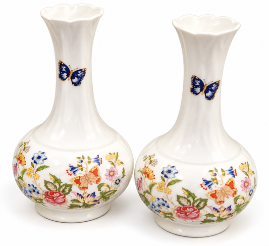 A pair of white ceramic budvases with a fluted neck and a colorful floral and butterfly pattern on the lower body, set against a plain white background.