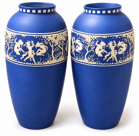 A pair of cobalt blue ceramic vases with cream-colored decorative bands depicting classical figures and trees, set against a plain white background.