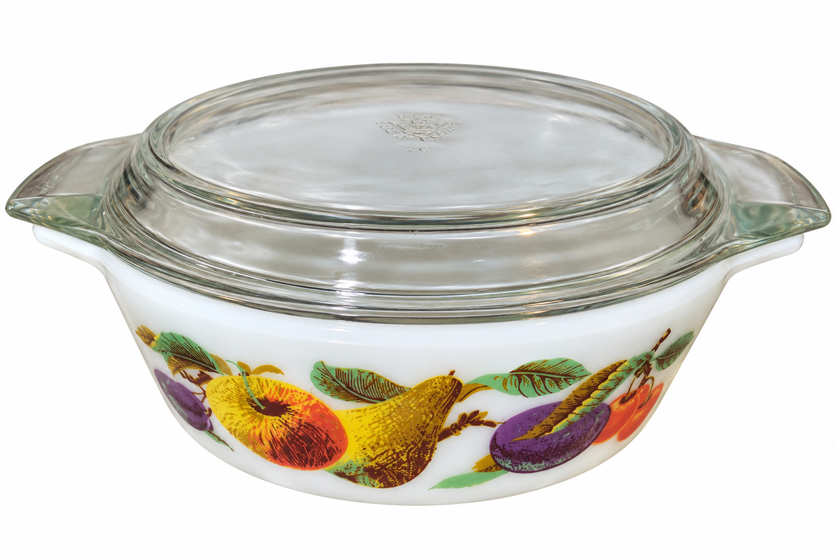 A vintage Pyrex glass casserole dish with a matching glass lid, featuring a white body decorated with a colorful fruit border pattern of pears, plums, and oranges.