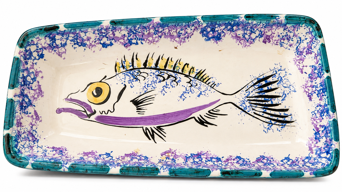 A rectangular ceramic serving tray with rounded corners, featuring a hand-painted fish design in purple, blue, black, and yellow on a cream-colored background, with a blue and purple speckled border.