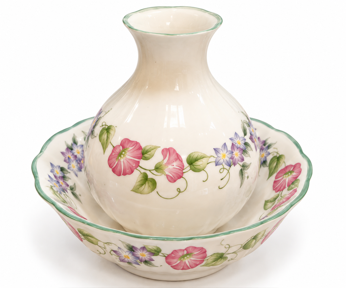 A ceramic floral vase with a matching scalloped bowl, featuring pink flowers and green leaves on a cream background, set against a plain white studio backdrop.